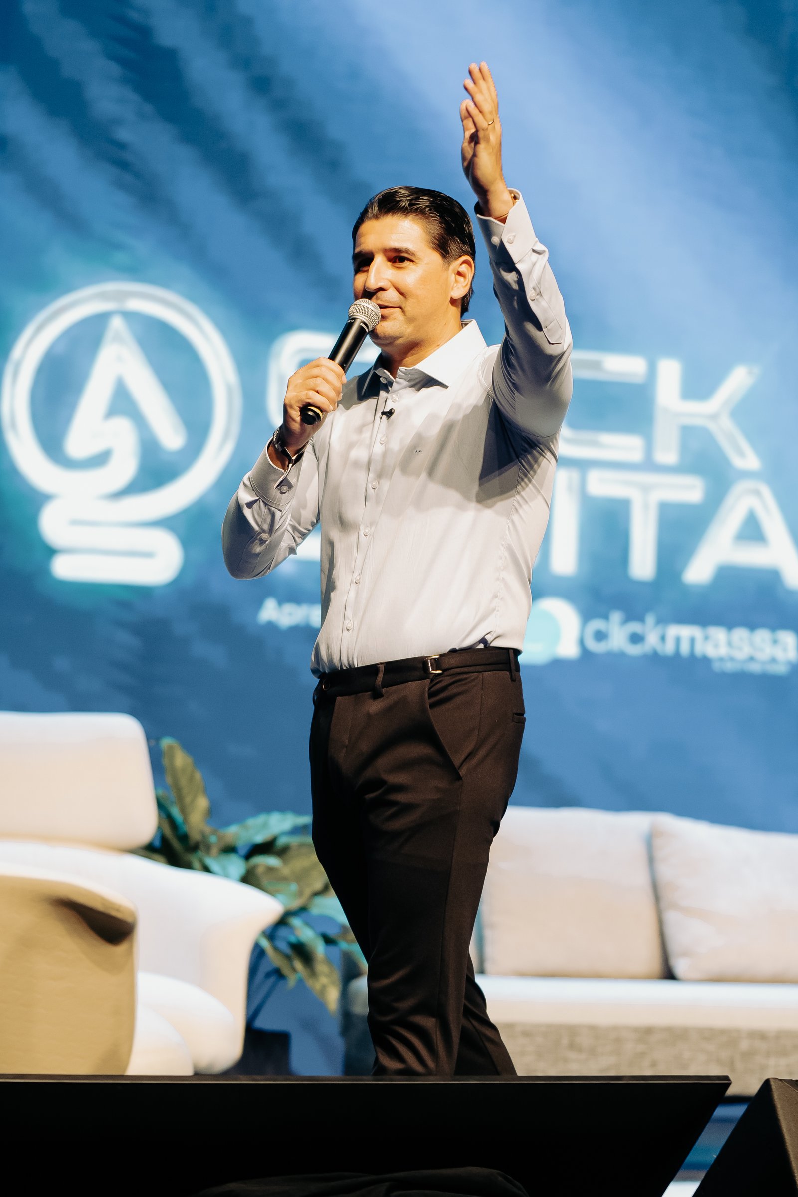 André Luz no palco com o microfone e o braço erguido durante uma palestra
